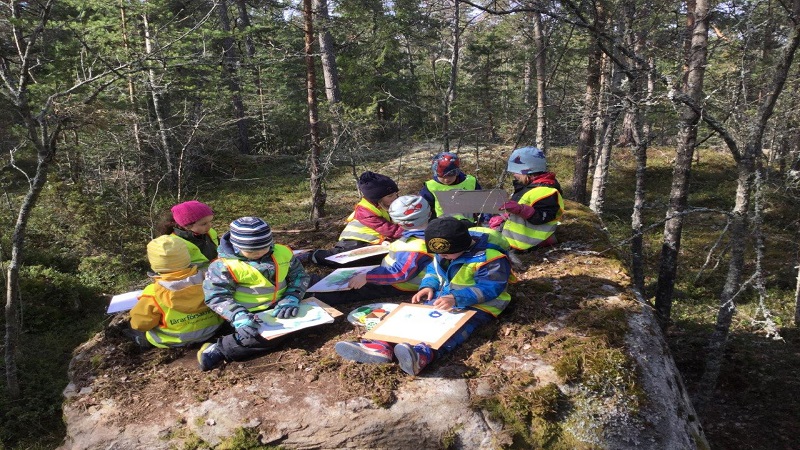 Barn sitter på en sten och läser.